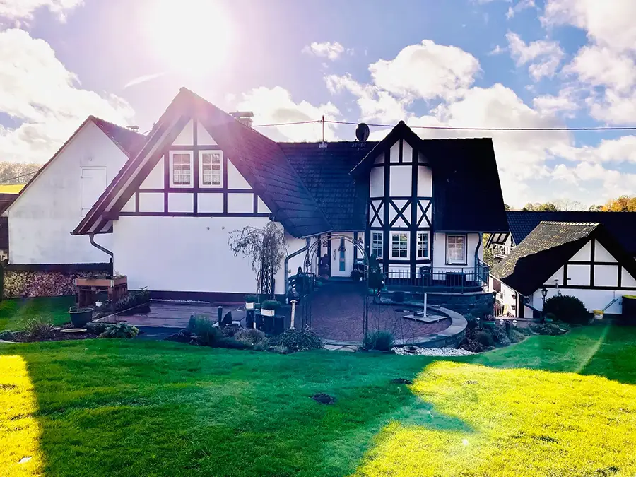 Objekt 19 Ein traditionelles schwarz-weißes Fachwerkhaus mit schrägem Dach, umgeben von einer grünen Wiese unter strahlender Sonne und blauem Himmel.